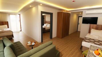 A hotel room with a green sofa, a small table with a fruit plate, a bed with a TV, and a wooden wardrobe.