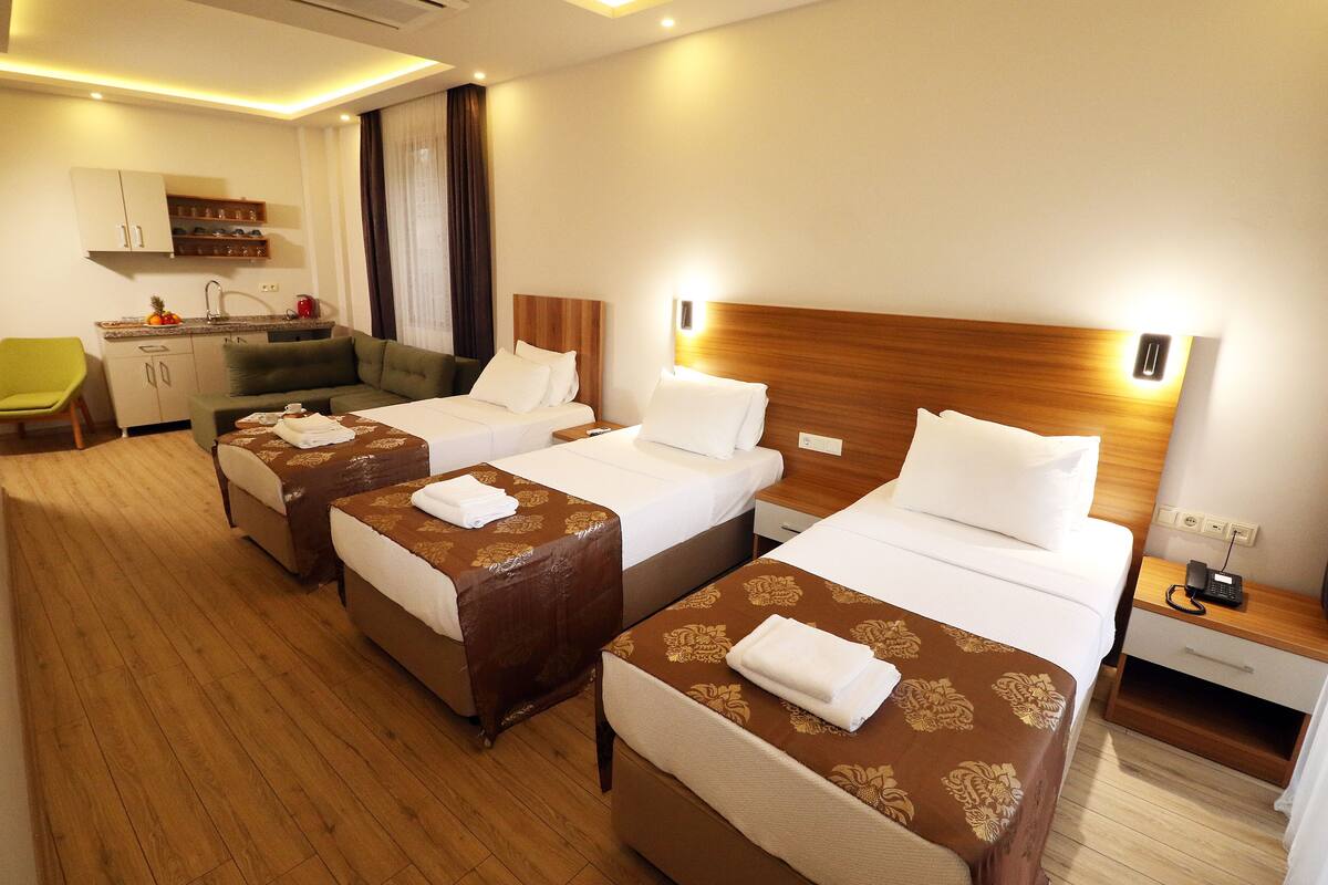 A hotel room with three single beds, a sofa, a small kitchenette, and a wooden floor.