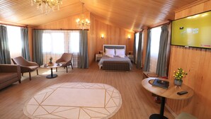 Une chambre d’hôtel avec un lit, deux fauteuils, une table basse ronde, un téléviseur et un plafond en bois.