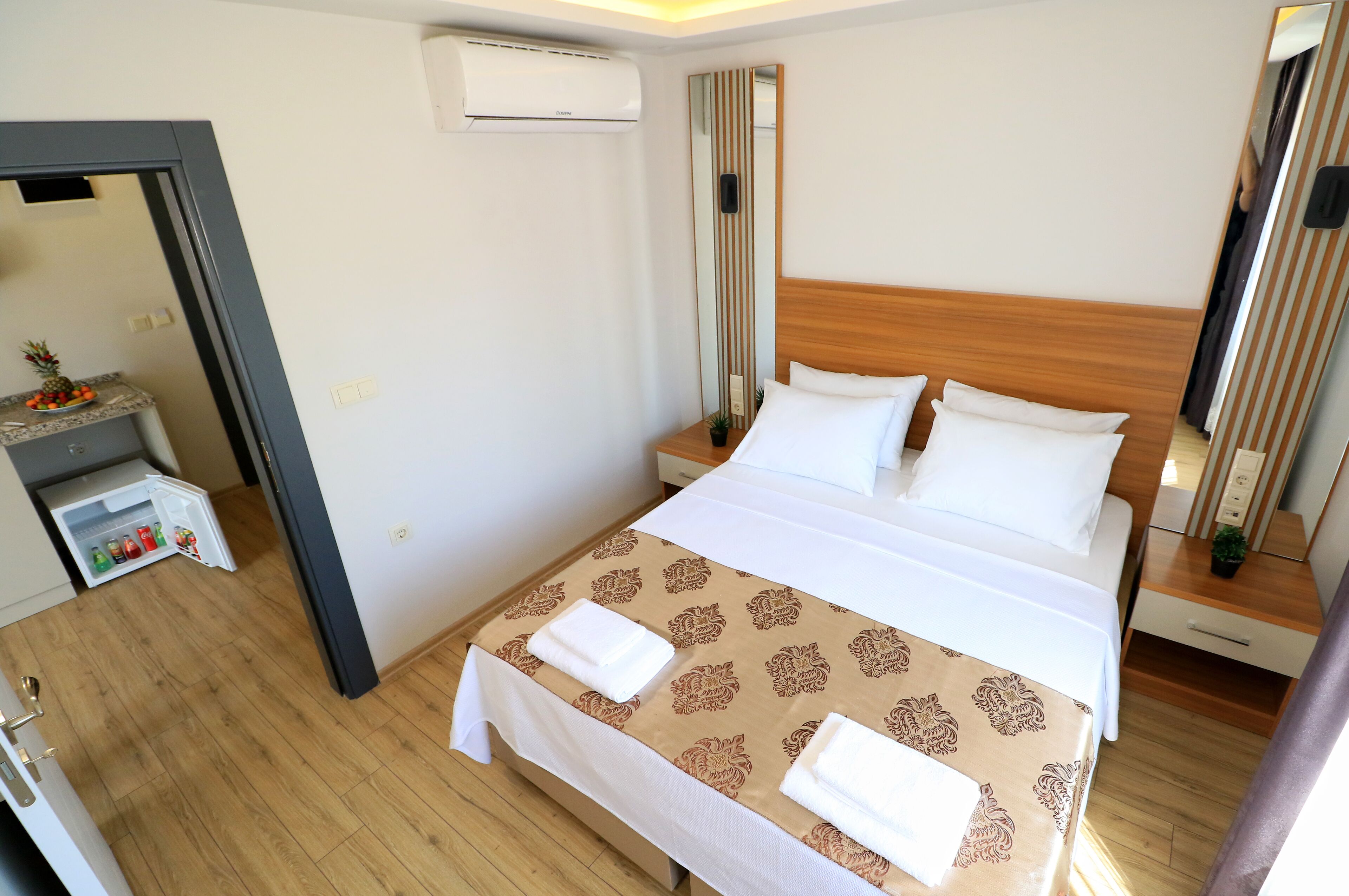 Une chambre d’hôtel comprenant un lit, une table de chevet, un miroir et un petit coin cuisine équipé d’un réfrigérateur.