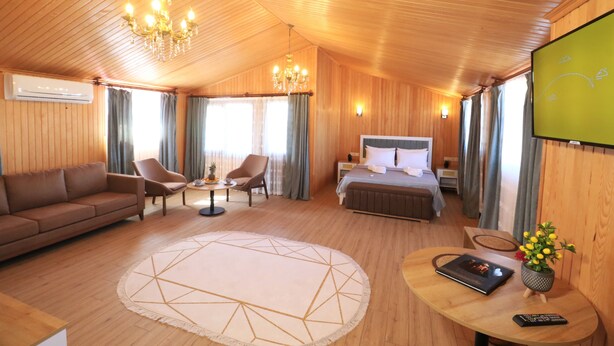 Une chambre d’hôtel avec un plafond en bois, un lit, un canapé, une chaise, une petite table, une télévision et une télécommande.