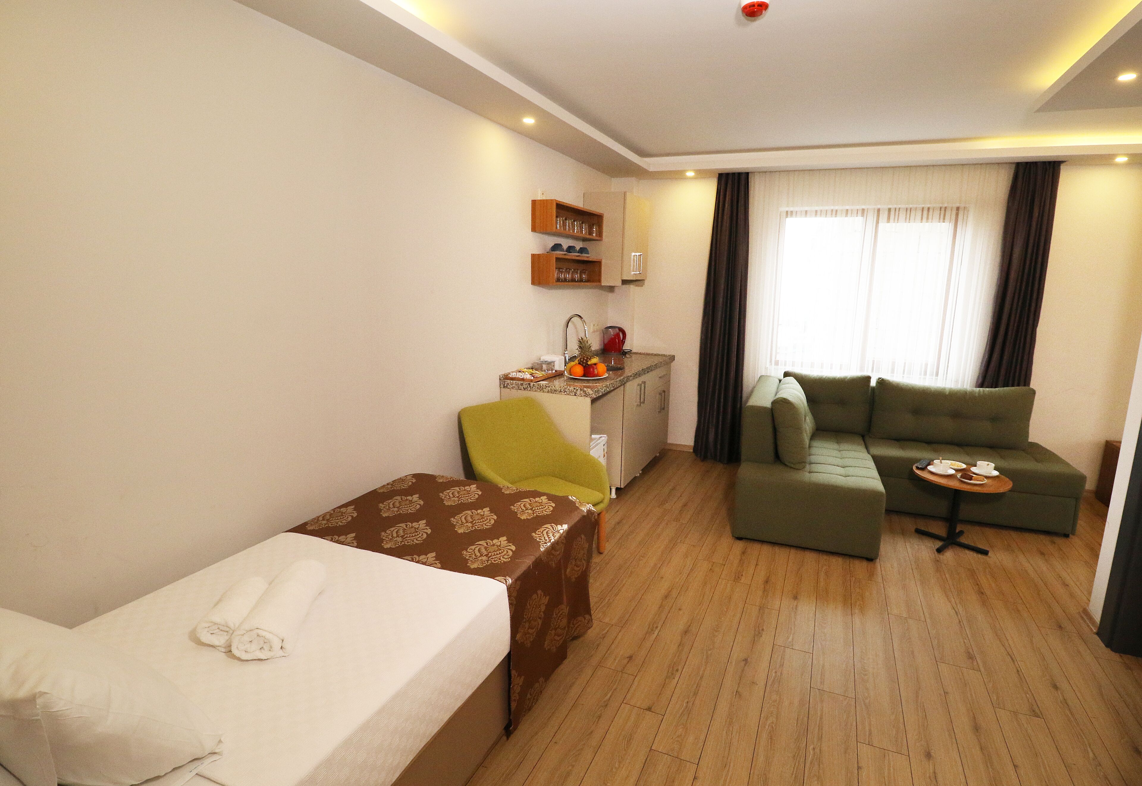 Une chambre d’hôtel avec un lit, une petite table, une chaise verte, un canapé et une fenêtre avec des rideaux.
