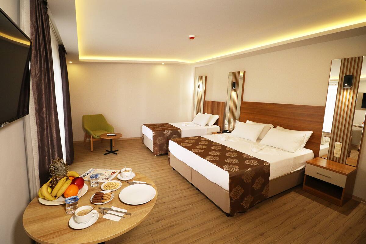 A hotel room with two beds, a dining table with breakfast, a TV, and a mirror.