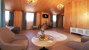 Une pièce aux murs lambrissés, avec une table ronde, deux fauteuils, un téléviseur et un lustre.