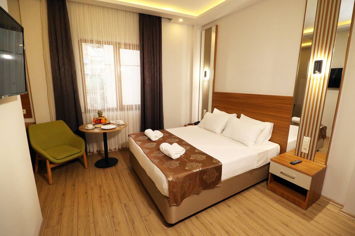 A hotel room with a bed, a green chair, a small table with a plate and a cup, and a TV on the wall.
