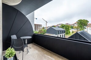En balkon med gelænder i sort, to fletstole, et rundt bord og en potteplante.