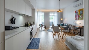 A modern kitchen with white cabinets, a dining area with a round table and chairs, and a bed with neatly made linens. - Nomad's Lux - Jardim à Vista (Porto)