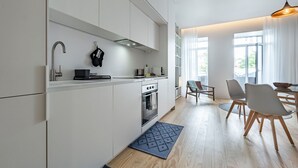 A modern kitchen with white cabinetry, a built-in oven, and a dining area with a table and chairs. - Nomad's Lux - Jardim à Vista (Porto)