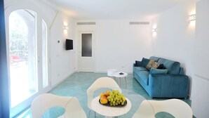 A bright living room with a blue sofa, a small white table with fruit, and a door leading to a balcony.