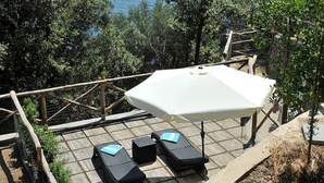 A deck with a white umbrella, two lounge chairs, and a view of the sea and a rocky island.