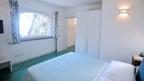 A bedroom with a bed, a window with curtains, a wardrobe, and a wall-mounted light fixture.