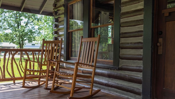 A wooden rocking chair on a porch with a view of a green landscape. - Rustic Charm with Modern Amenities, Two Creeks Crossing Resort (Livingston)