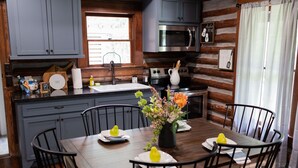 A kitchen with grey cabinets, a stainless steel microwave, and a sink. There is a dining table with chairs and a vase of flowers. - Rustic Charm with Modern Amenities, Two Creeks Crossing Resort (Livingston)