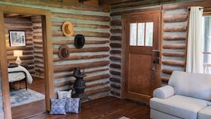 A log cabin interior with a sofa, a fireplace, and a door. - Rustic Charm with Modern Amenities, Two Creeks Crossing Resort (Livingston)