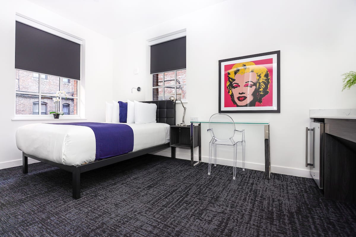 A modern bedroom with a bed, a desk, and a framed pop art print on the wall.