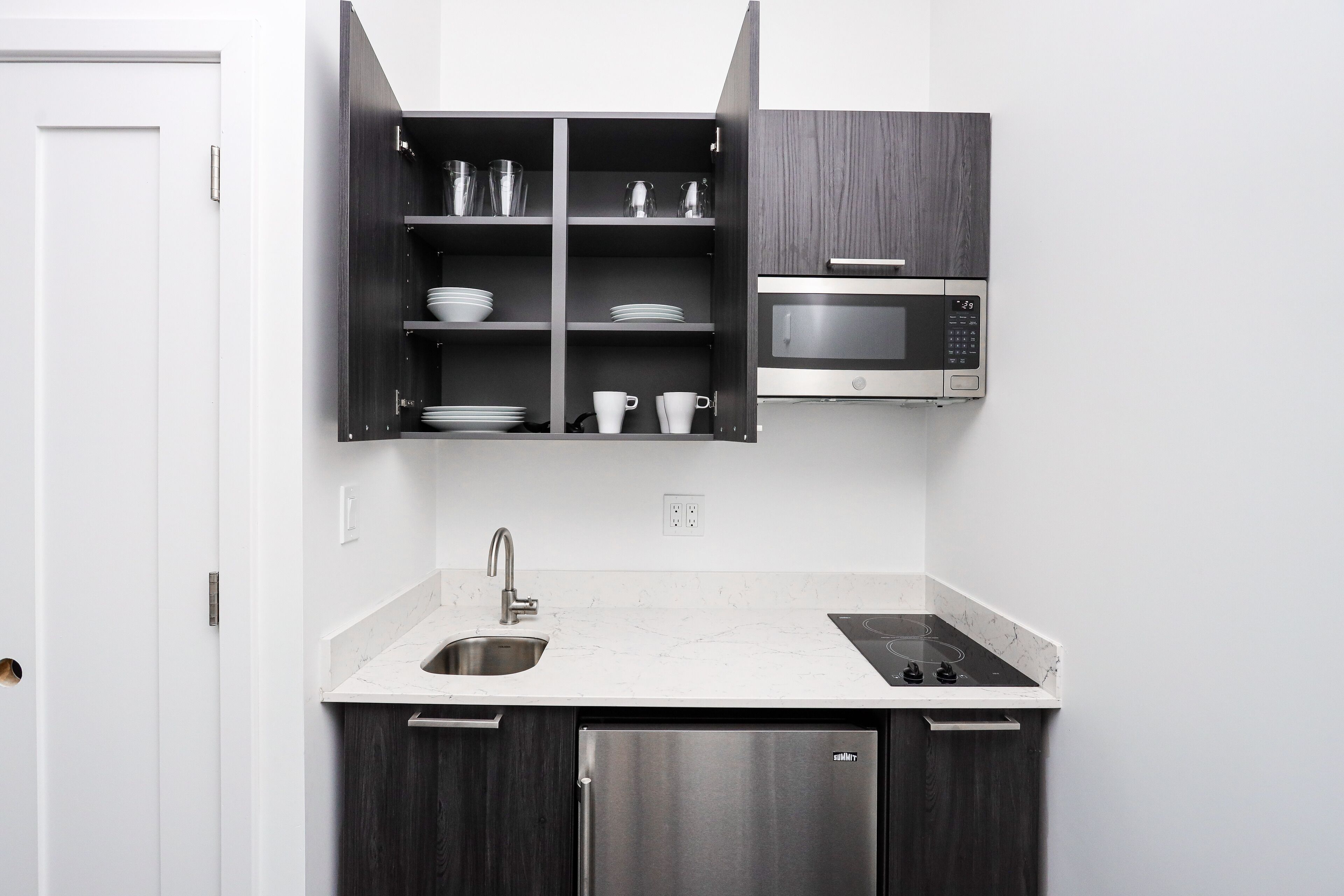 Una cocina moderna con microondas integrado, refrigerador de acero inoxidable y encimera de mármol.