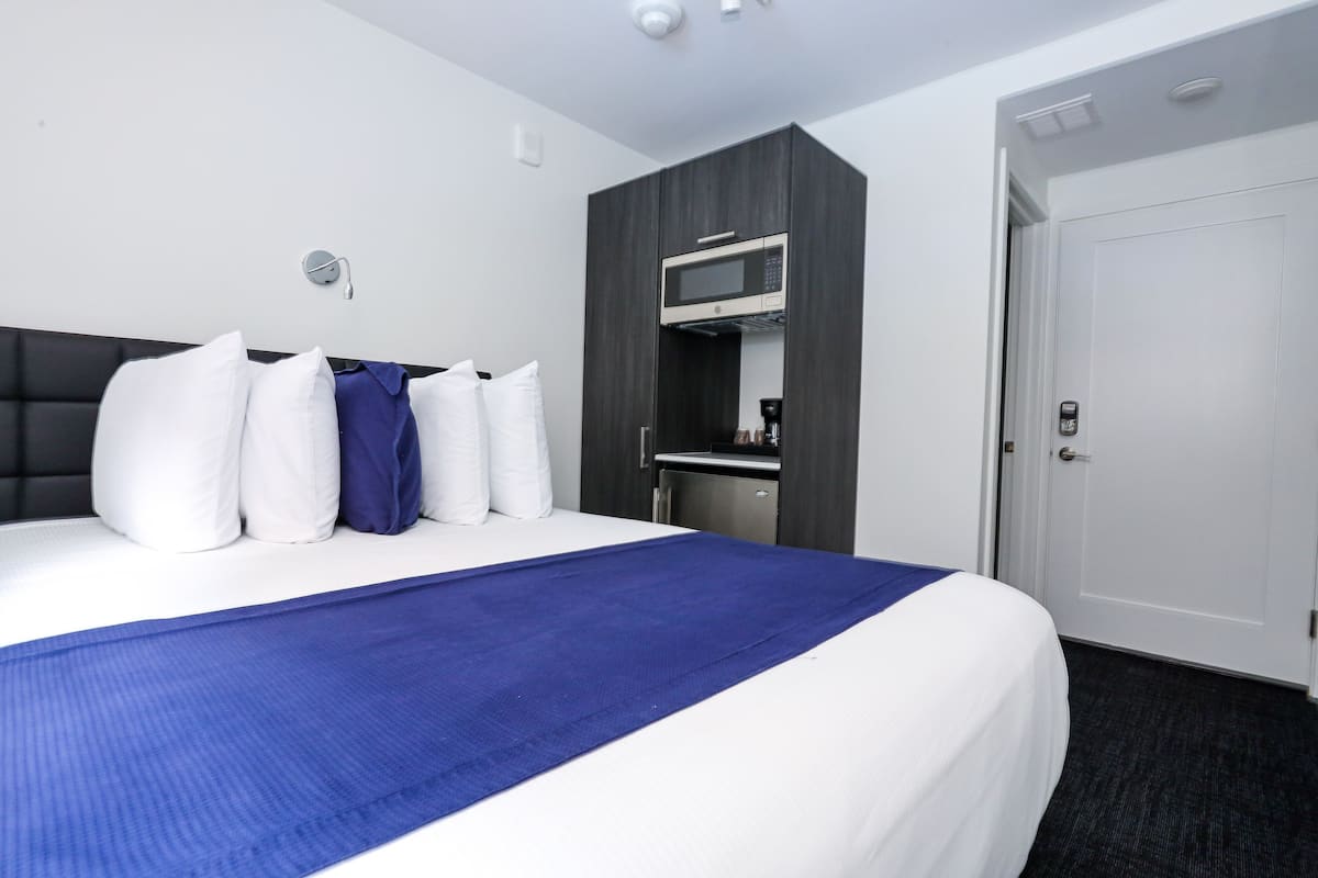 A hotel room with a large bed, a microwave, a coffee machine, and a door.