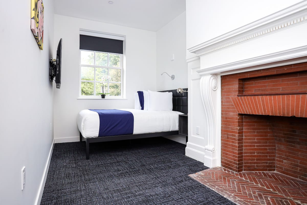 A bedroom with a bed, a window, a fireplace, and a wall-mounted TV.