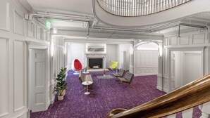 Un hall d’entrée spacieux, doté d’un tapis violet, d’une cheminée, de meubles modernes et d’un grand escalier.