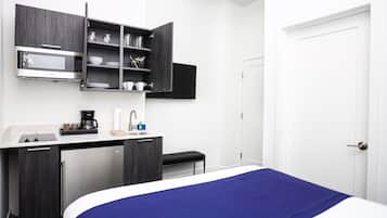 A compact hotel room with a bed, a desk with a microwave, a coffee maker, and a small refrigerator.
