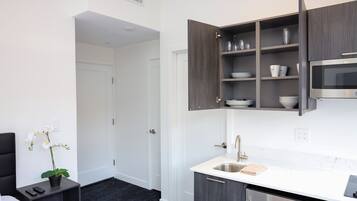 A compact hotel kitchen with a built-in microwave, a sink, and dark wooden cabinets.