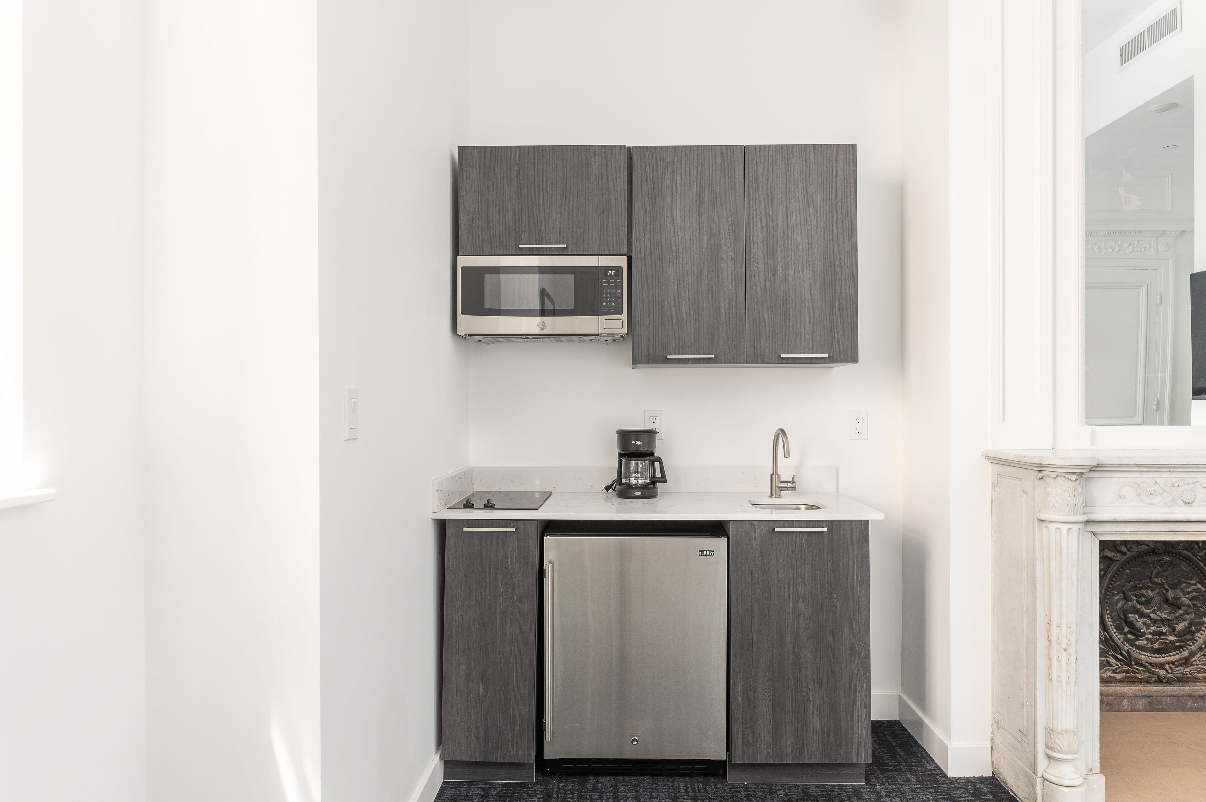 A compact kitchen with a built-in microwave, a coffee maker, and a refrigerator.