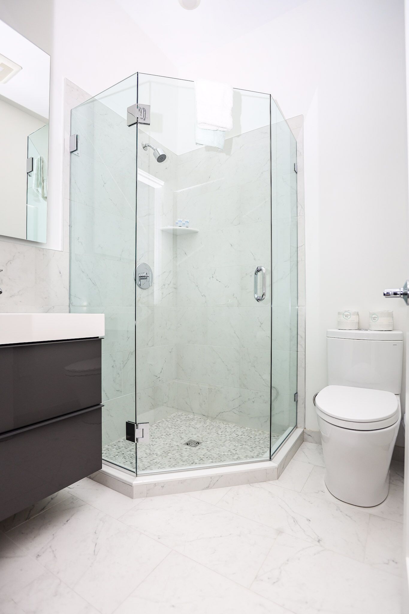 Een moderne badkamer met een douchecabine van glas, een wit toilet en een vloer van marmer.