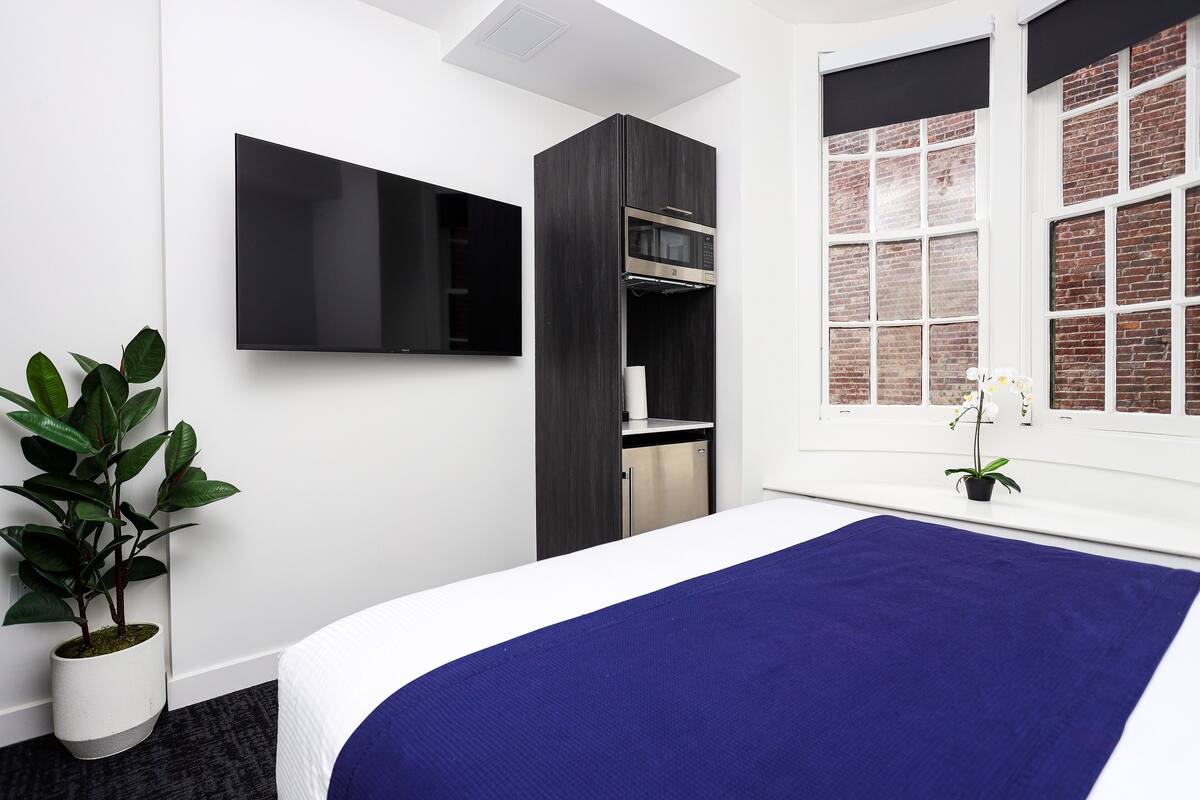 A modern hotel room with a large bed, a flat-screen TV, a built-in microwave, and a small kitchenette.