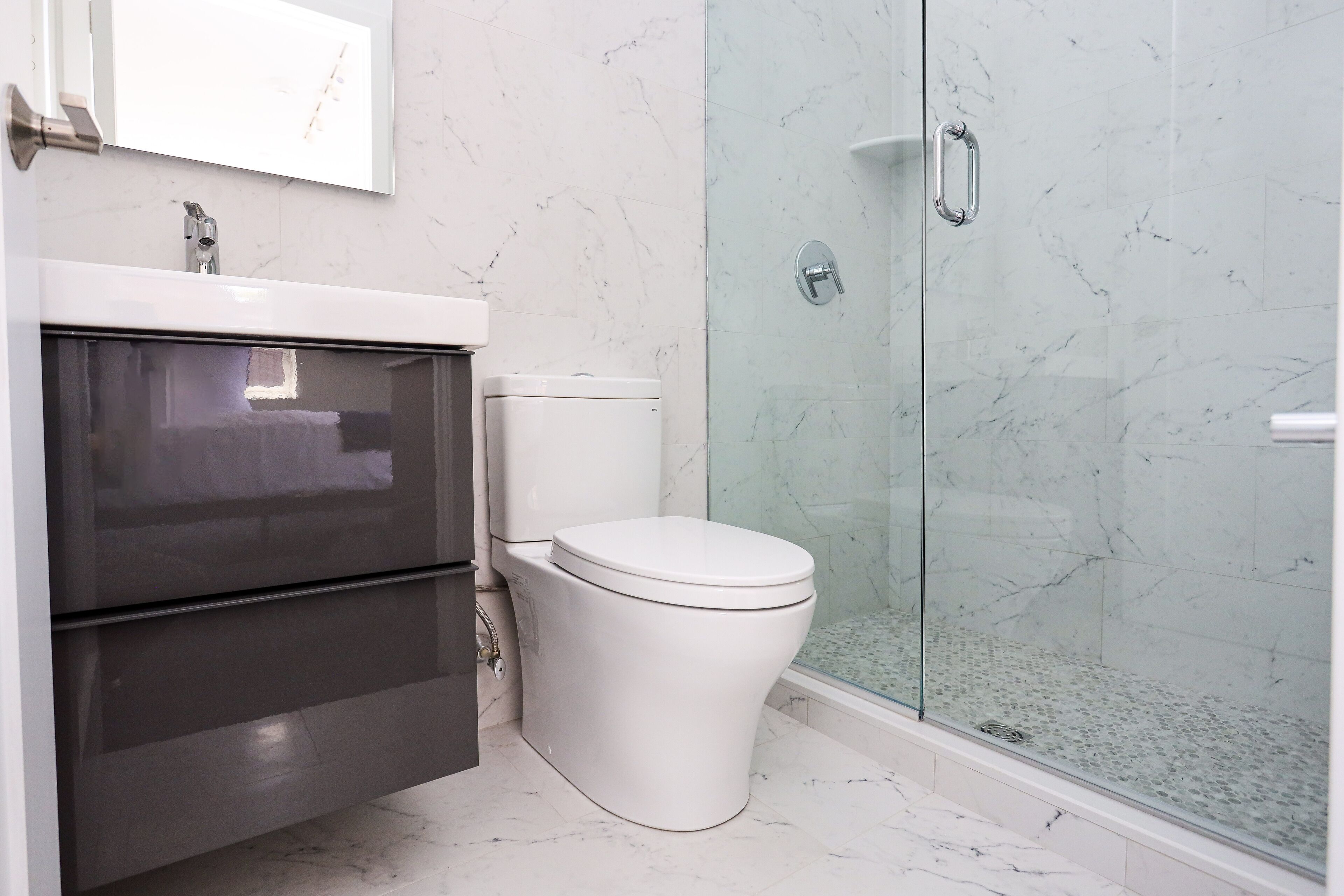 A modern bathroom with a glass-enclosed shower, a white toilet, and a stainless steel sink.