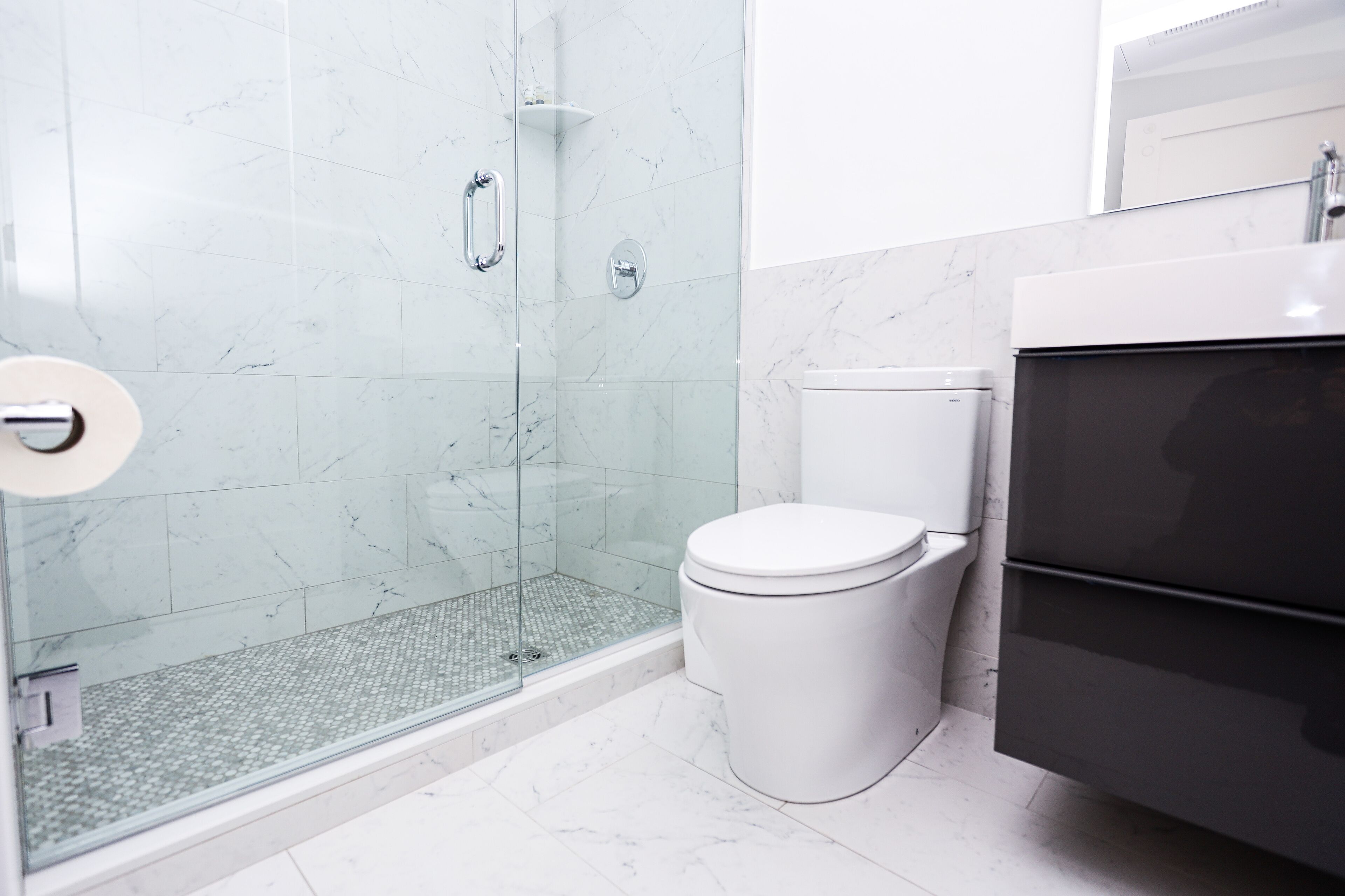 A modern bathroom with a glass-enclosed shower, a toilet, and a dark-colored vanity.