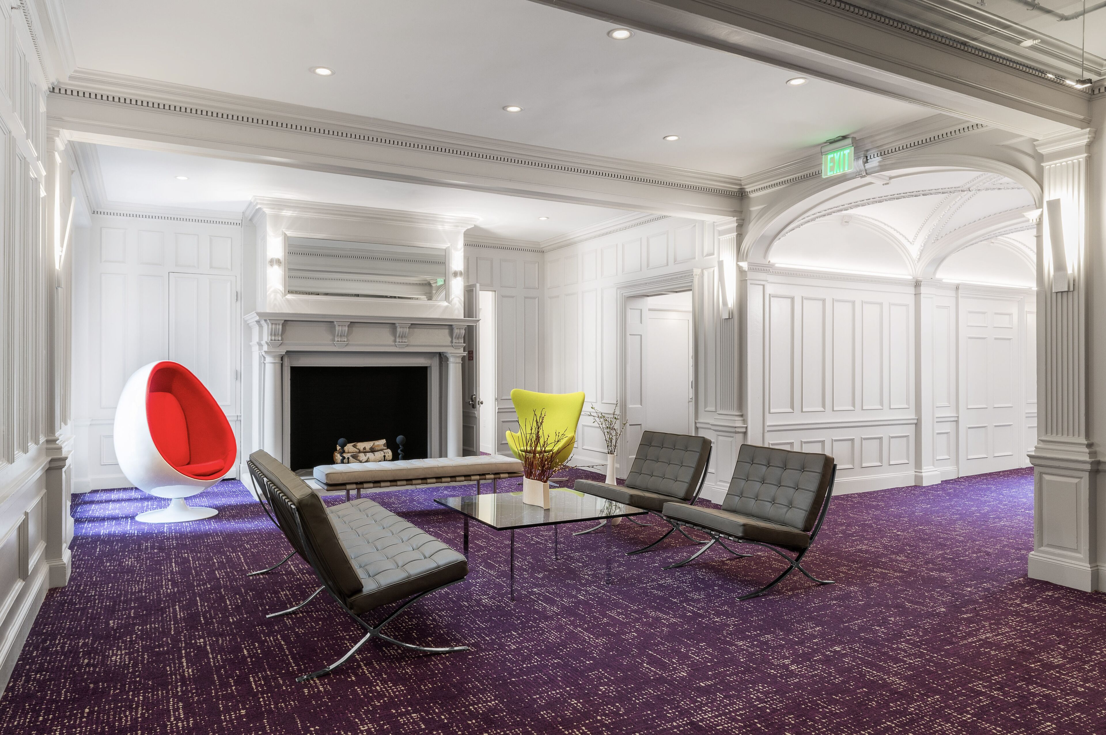 A conference room with a glass table, four chairs, a fireplace, and white paneled walls.