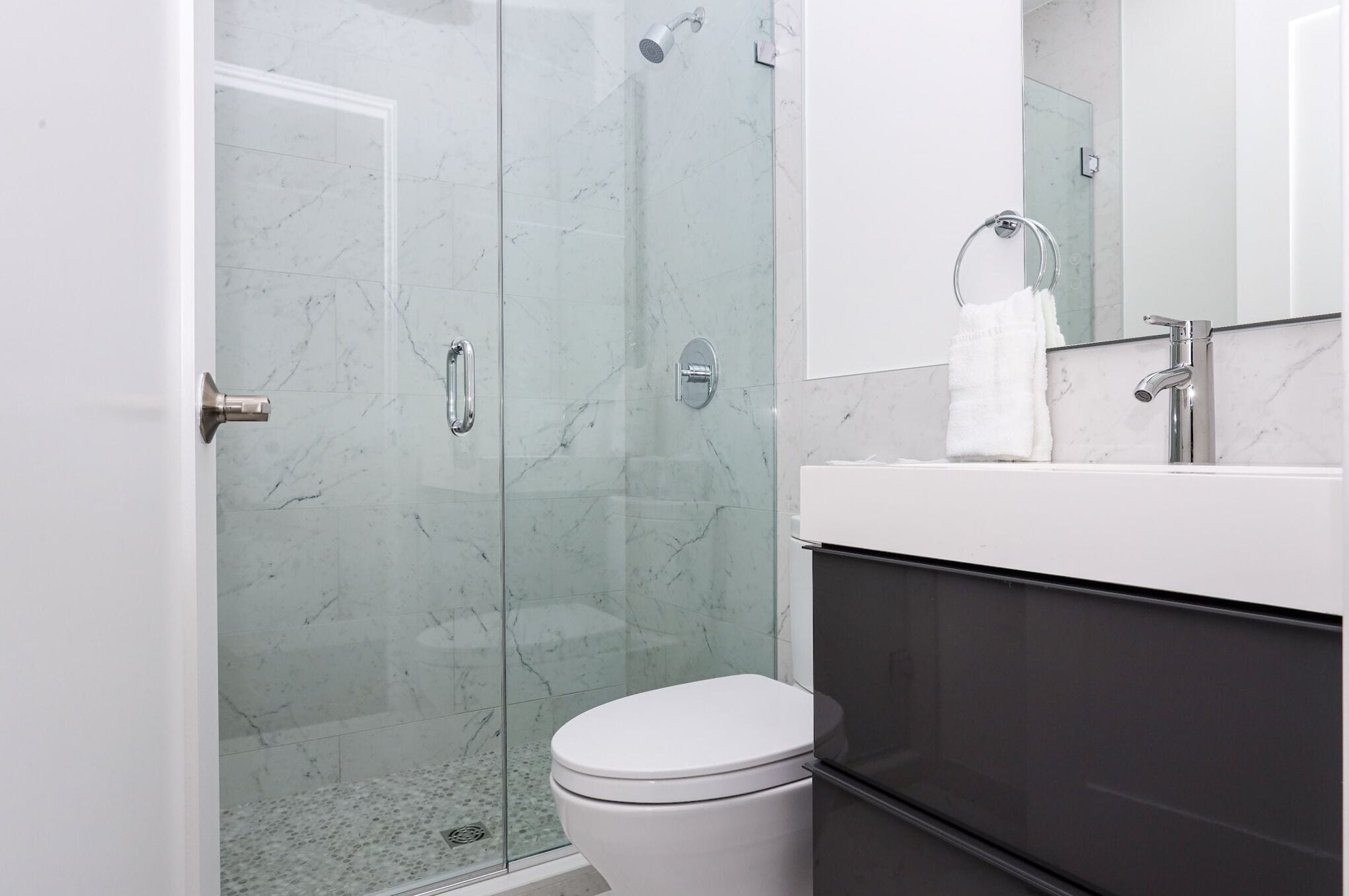 A modern bathroom with a glass shower enclosure, a white toilet, and a sink with a towel ring.
