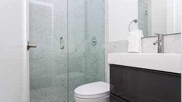 A modern bathroom with a glass shower enclosure, a white toilet, and a sink with a towel ring.