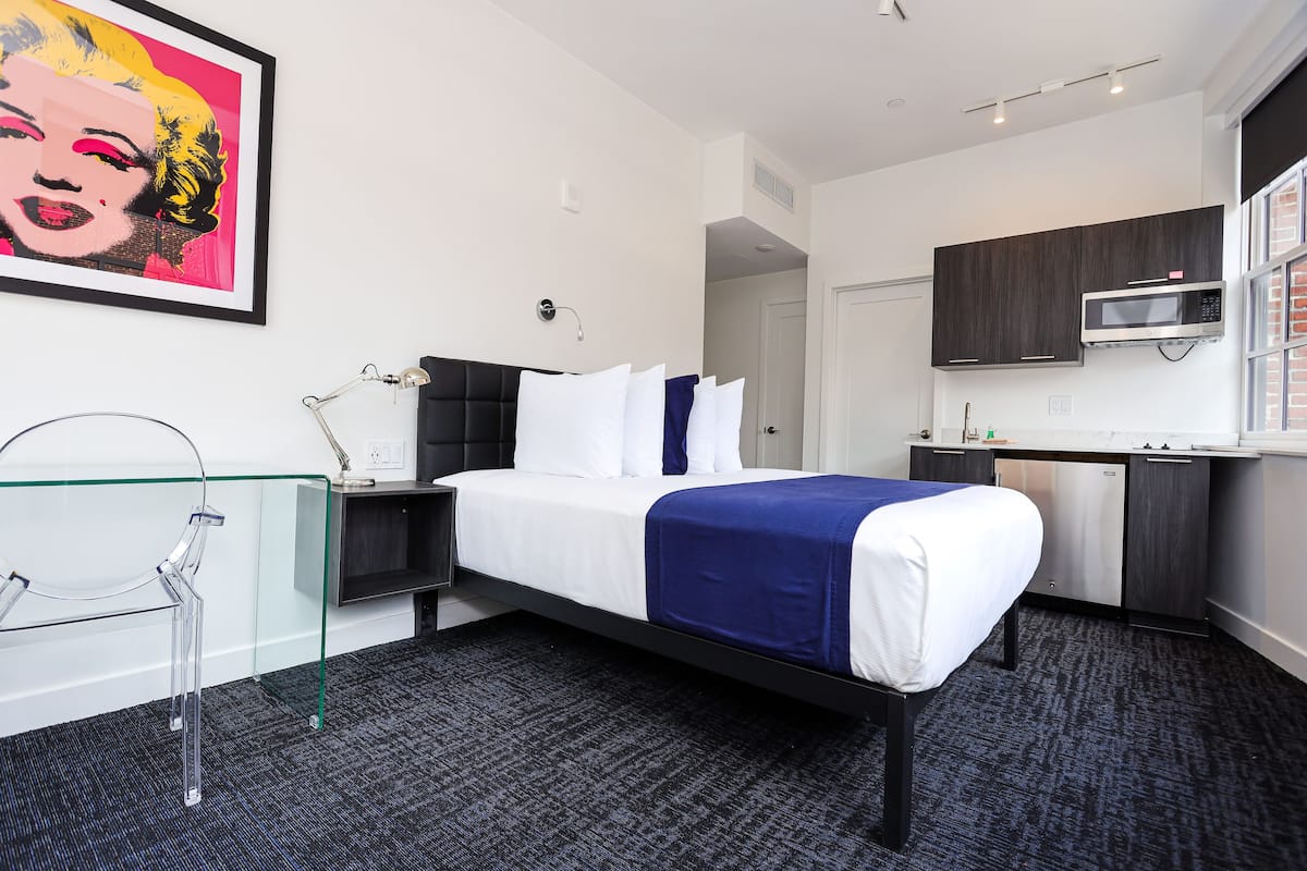A modern hotel room with a bed, a desk, a microwave, and a bathroom.