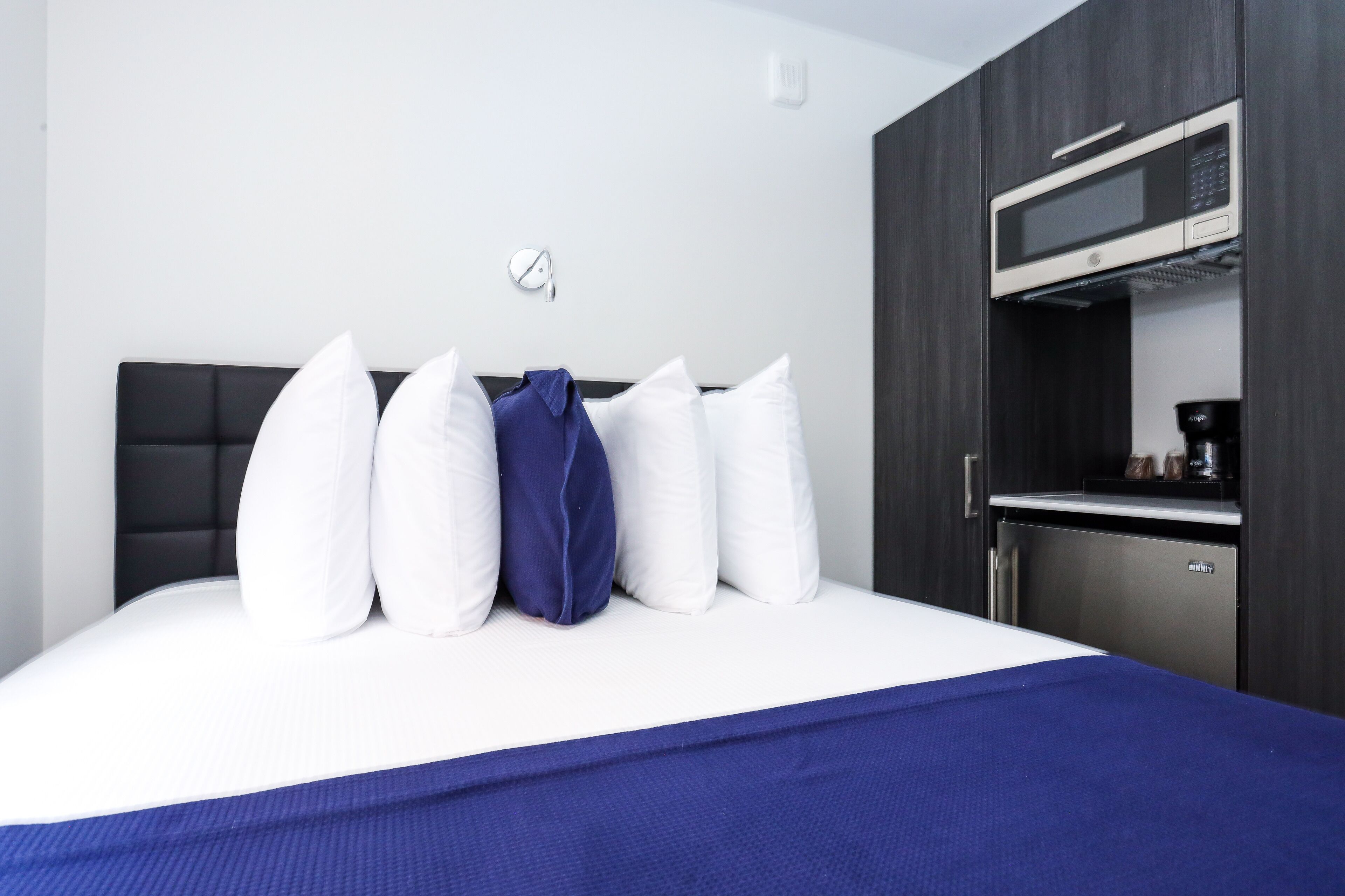 Een hotelkamer met een bed, kussens, een blauw sprei, een magnetron en een koffieapparaat.
