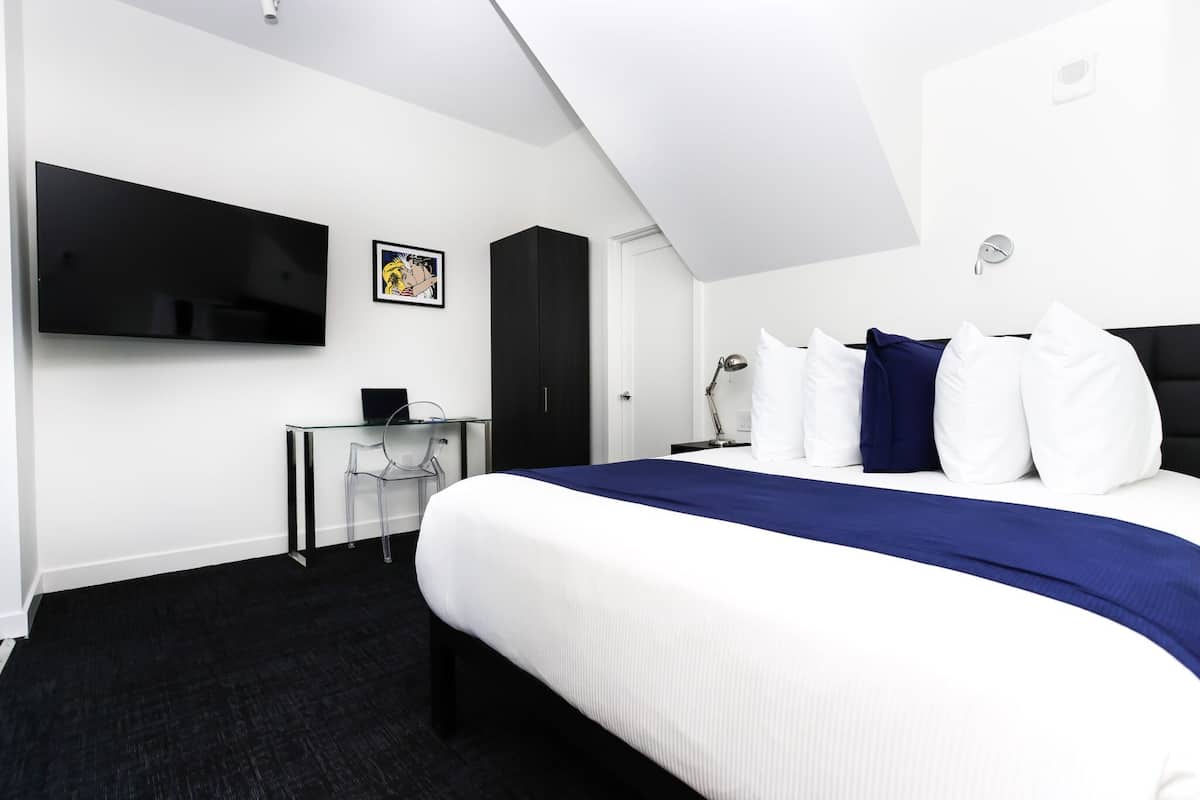 A hotel room with a bed, a desk, a chair, a flat-screen TV, and a wardrobe.