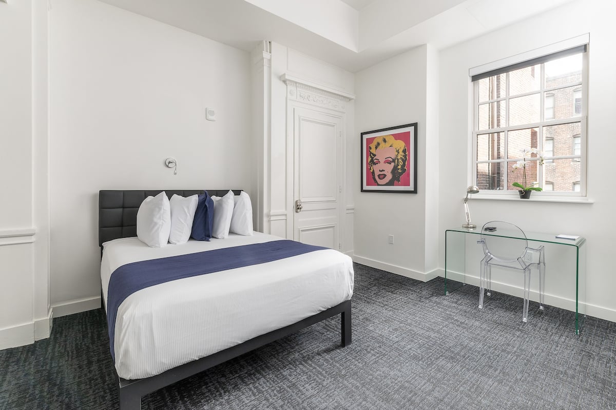 A bedroom with a bed, a desk, and a window.