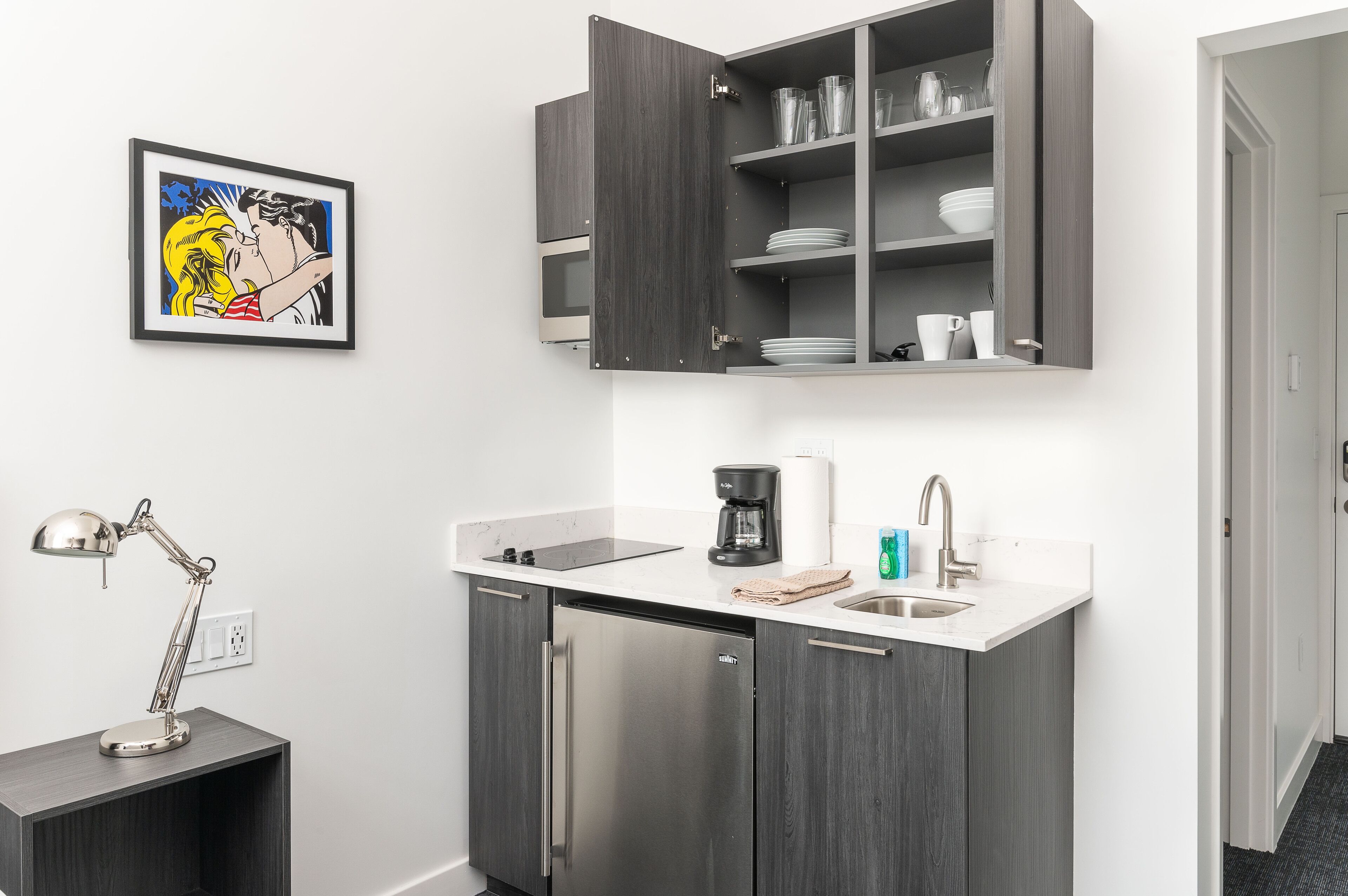 Una cocina compacta con lavavajillas integrado, cafetera y pileta.