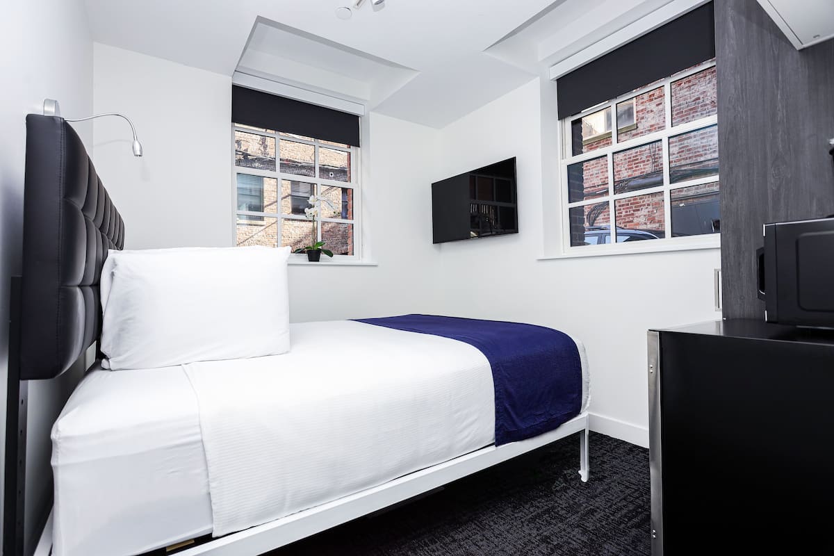 A modern bedroom with a bed, a desk, and two windows.