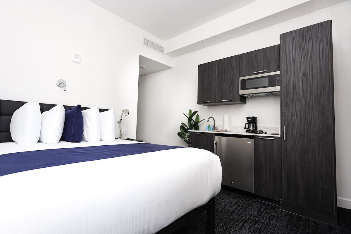 A hotel room with a bed, a small kitchenette, and a dark wood cabinet.