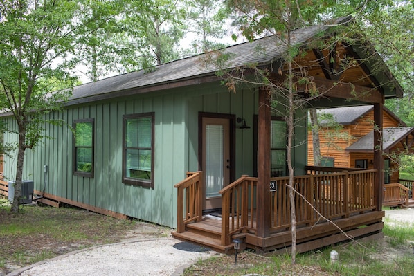 A small, single-story cabin with a porch and a door, surrounded by trees.
