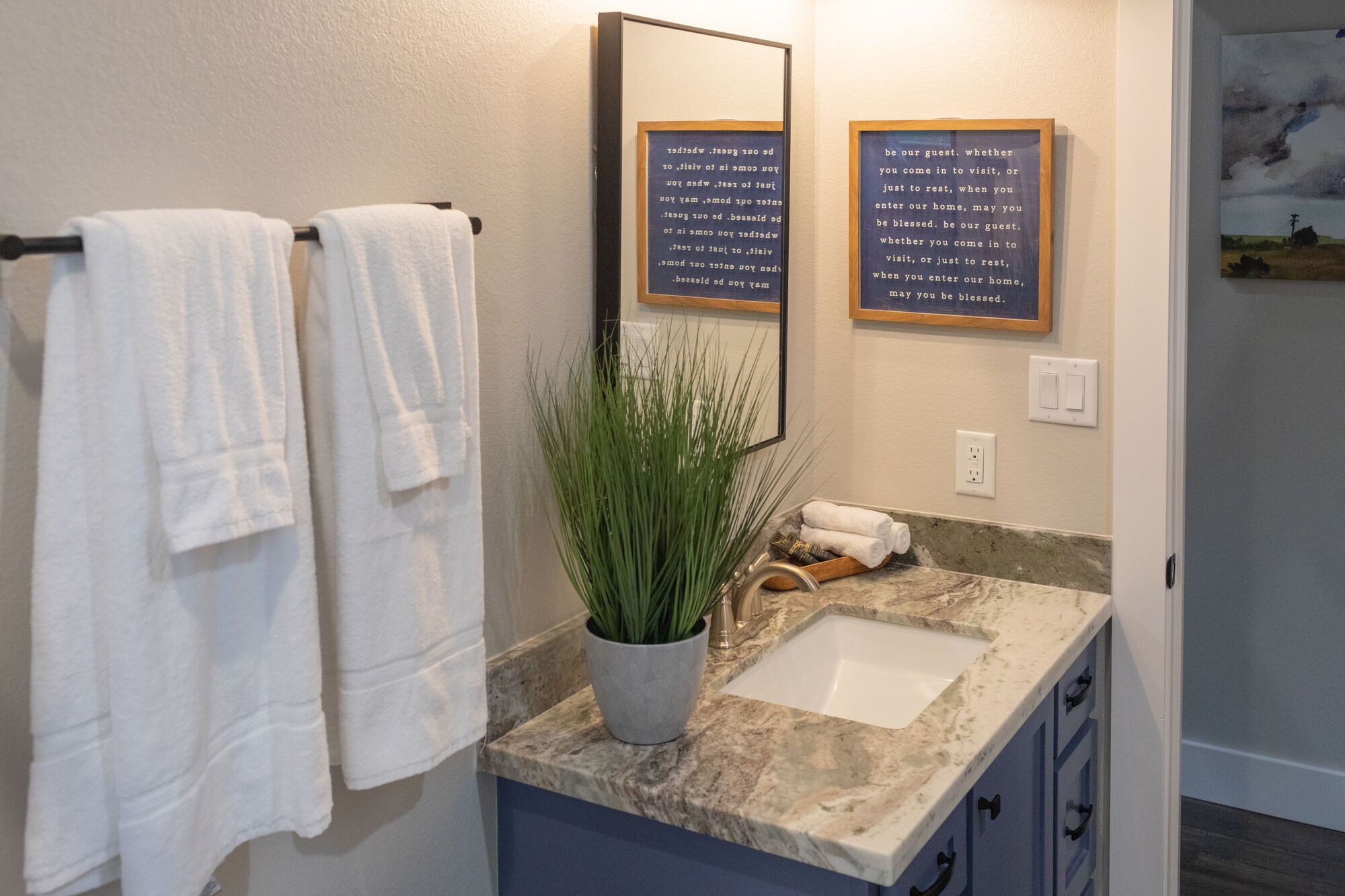 A bathroom with a sink, two towels, a mirror, and two framed quotes on the wall.