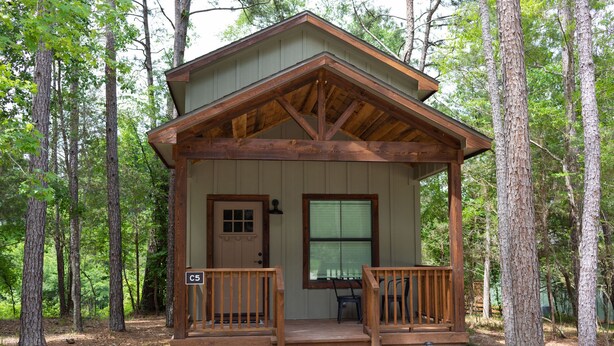 A cabin with a porch, a door, and a window. - Cozy, Spacious, and Right on the Banks of Rocky Creek, Two Creeks Crossing Resort (Livingston)