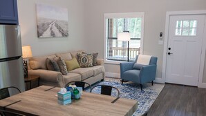 A living room with a beige sofa, a blue armchair, a wooden coffee table, and a patterned rug. - Cozy, Spacious, and Right on the Banks of Rocky Creek, Two Creeks Crossing Resort (Livingston)