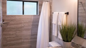 A modern bathroom with a shower, a toilet, a sink with a marble countertop, a potted plant, and a mirror. - Cozy, Spacious, and Right on the Banks of Rocky Creek, Two Creeks Crossing Resort (Livingston)