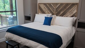 Un lit bien fait, avec une couvre-lit bleue et blanche, une tête de lit en bois et un banc au pied du lit.