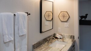 Une salle de bain avec un lavabo en marbre, deux miroirs fixés au mur et deux horloges murales hexagonales.