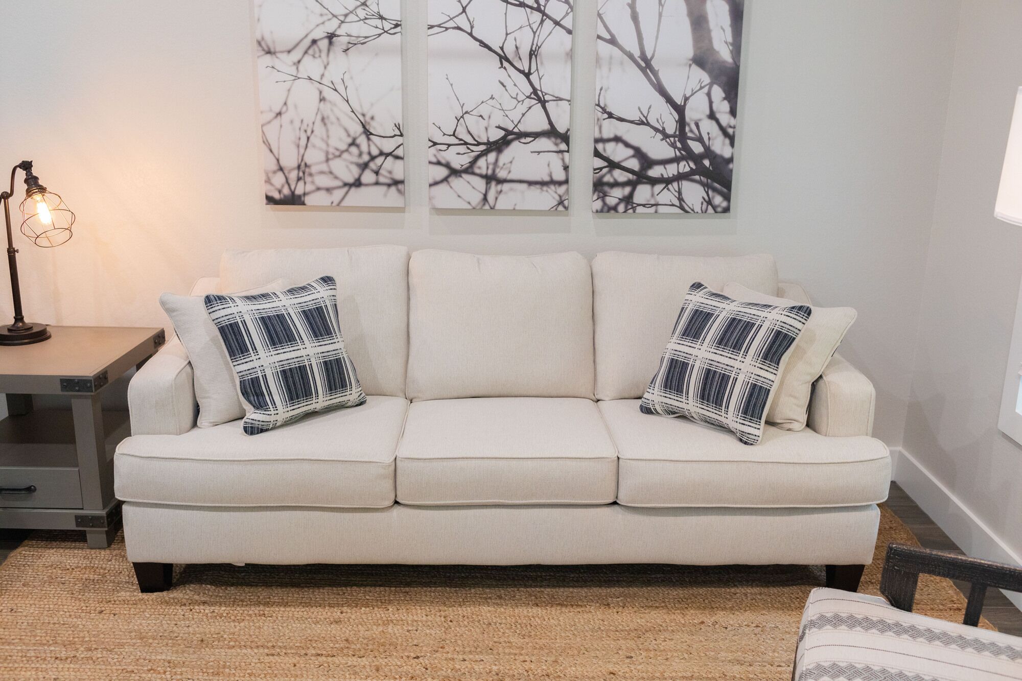 Un sofá color beige con dos almohadones estampados, una lámpara y una pared decorada con motivos abstractos de ramas de árboles.