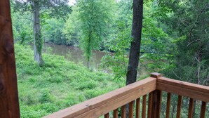 A wooden deck overlooking a river surrounded by dense forest. - Cozy, Spacious, and Right on the Banks of Rocky Creek, Two Creeks Crossing Resort (Livingston)