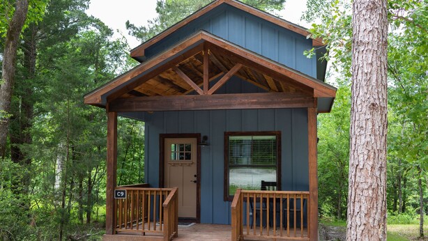 A cabin with a wooden deck, a front door, and two windows. - Cozy, Spacious, and Right on the Banks of Rocky Creek, Two Creeks Crossing Resort (Livingston)
